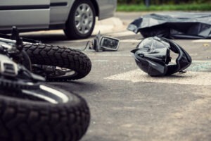 A helmet lies on the road next to a damaged motorcycle after a collision with a car. A motorcycle accident lawyer in Poquoson will help injured riders build a strong claim.