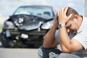 A driver sits on the road holding his head after being involved in a car crash. A lawyer can tell him what to do after the car accident to protect the value of his claim.
